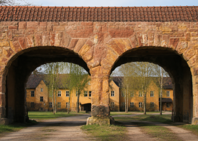 Entrada exterior de Hillersleben, con dos arcos de piedra, tejado de teja y edificios históricos al fondo.