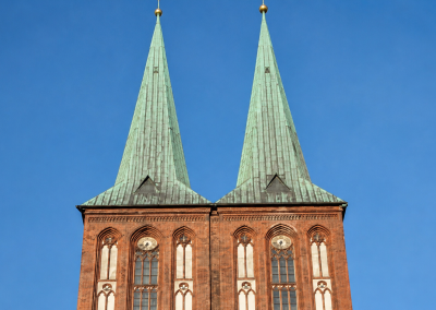 Dos torres de la Nikolaikirche con agujas verdes, fachada de ladrillo, ventanas góticas y cielo azul despejado.