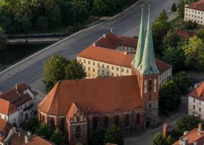 Vista general de la Nikolaikirche, con sus torres gemelas, tejado rojizo y entorno urbano junto al agua.