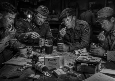 Soldados de la Segunda Guerra Mundial tomando Pervitin en una tienda de campaña, sentados alrededor de una mesa con mapas, tazas, cajas y comprimidos.