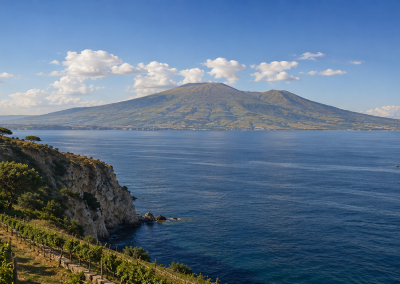 Acantilados de Sorrento con vegetación mediterránea, viñedos, mar azul y el Vesubio al fondo sobre el golfo de Nápoles.